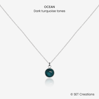 6mm fused glass circular cabochon set into a steel base and attached to a 400mm stainless steel pendant chain via jump ring. Cabochon colour: Ocean = deep turquoise and aqua marble effect.