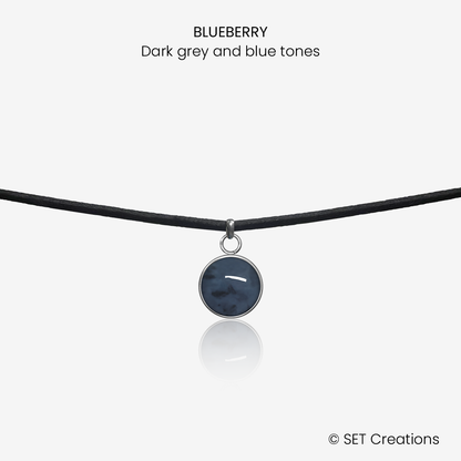 10mm fused glass circular cabochon set into a steel base and attached to a 380mm faux suede black cord via jump ring. Cabochon colour: Blueberry = dark grey and blue marble effect.