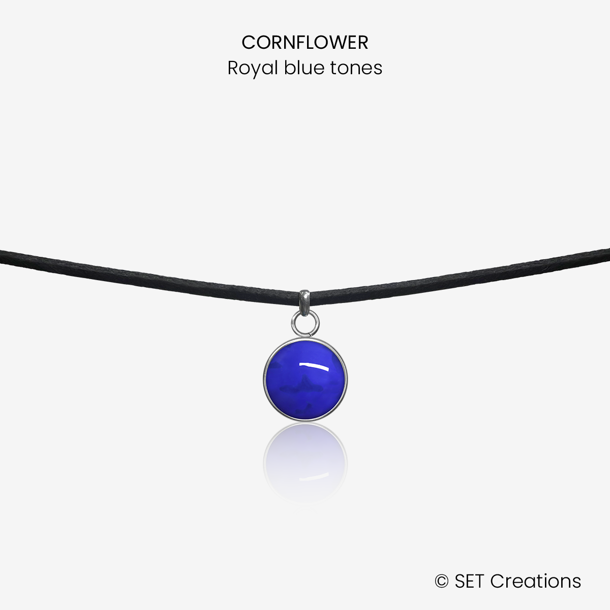10mm fused glass circular cabochon set into a steel base and attached to a 380mm faux suede black cord via jump ring. Cabochon colour: Cornflower = royal blue marble effect.