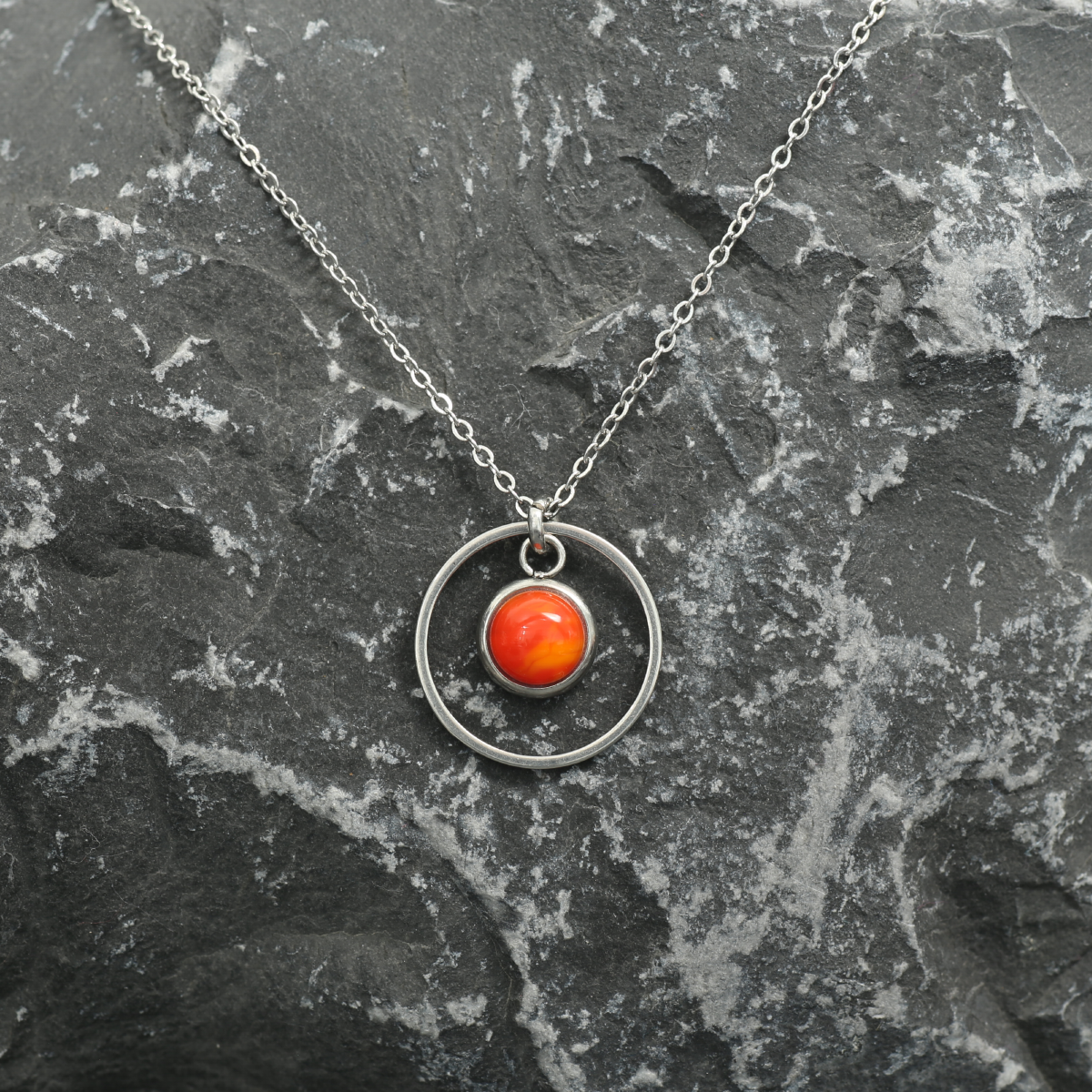 6mm fused glass circular cabochon set into a steel base, framed with a 16mm steel hoop and attached to a 400mm stainless steel pendant chain via jump ring. Cabochon colour: Sunrise = orange and deep red marble effect.