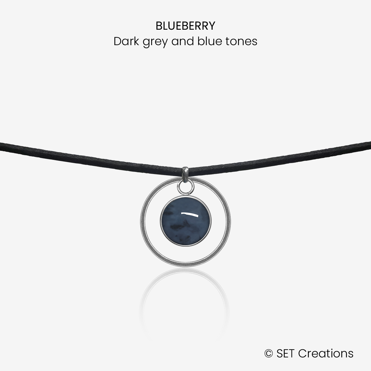10mm fused glass circular cabochon set into a steel base, framed with a 20mm steel hoop and attached to a 380mm faux suede black cord via jump ring. Cabochon colour: Blueberry = dark grey and blue marble effect.