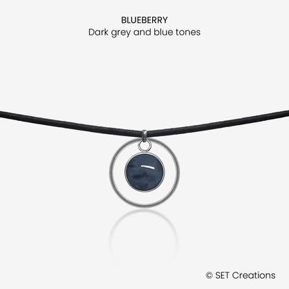 10mm fused glass circular cabochon set into a steel base, framed with a 20mm steel hoop and attached to a 380mm faux suede black cord via jump ring. Cabochon colour: Blueberry = dark grey and blue marble effect.