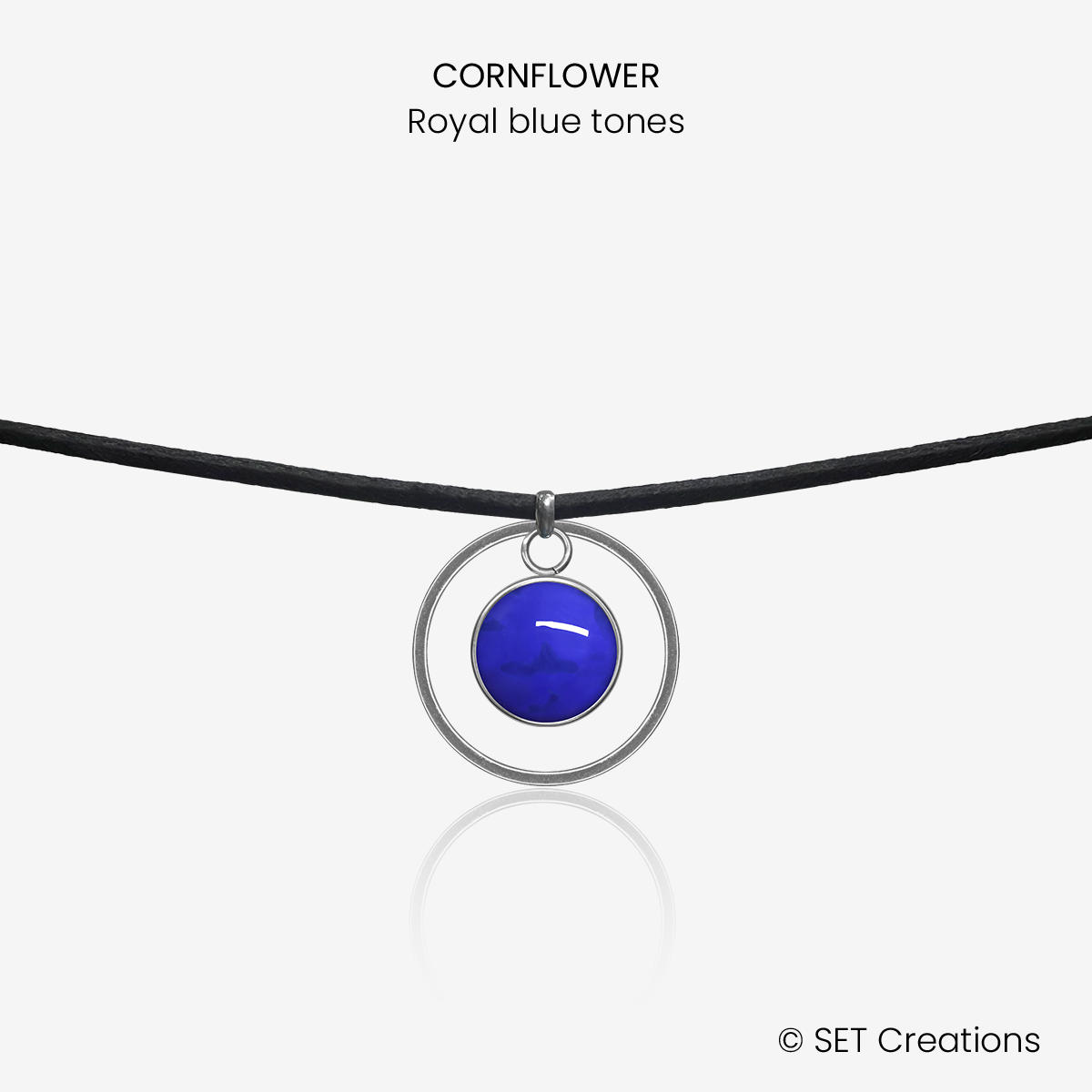 10mm fused glass circular cabochon set into a steel base, framed with a 20mm steel hoop and attached to a 380mm faux suede black cord via jump ring. Cabochon colour: Cornflower = royal blue marble effect.