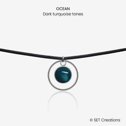 10mm fused glass circular cabochon set into a steel base, framed with a 20mm steel hoop and attached to a 380mm faux suede black cord via jump ring. Cabochon colour: Ocean = deep turquoise and aqua marble effect.