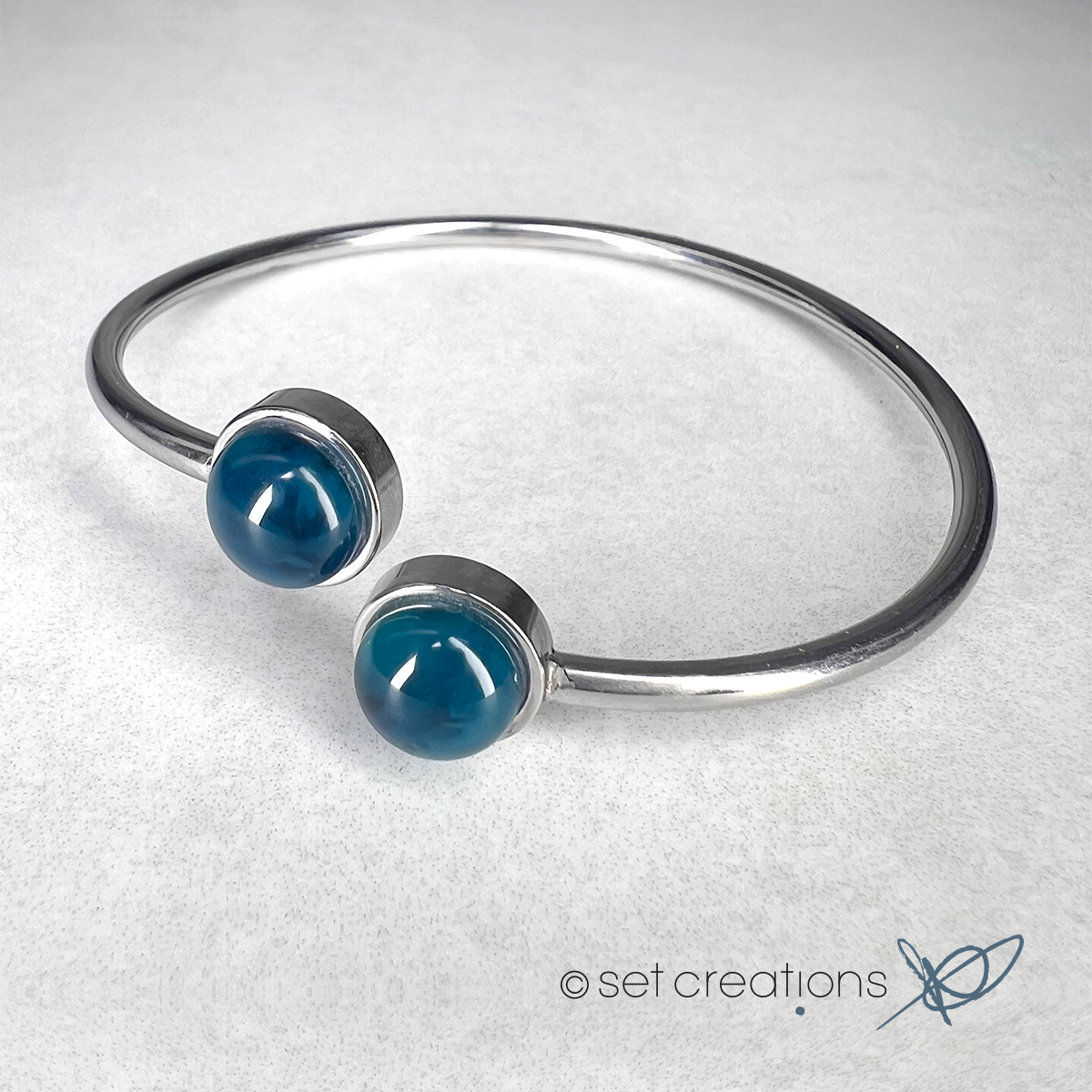 2 x 8mm fused glass circular cabochons set into stainless steel adjustable 2mm thick wire bangles. Cabochon colour: Ocean = deep turquoise and aqua marble effect.