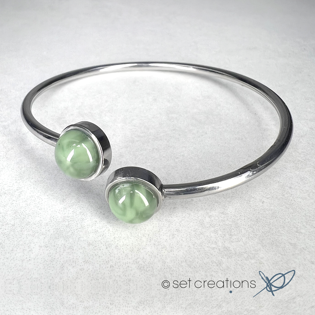 2 x 8mm fused glass circular cabochons set into stainless steel adjustable 2mm thick wire bangles. Cabochon colour: Olive = pale and subtle green marble effect.