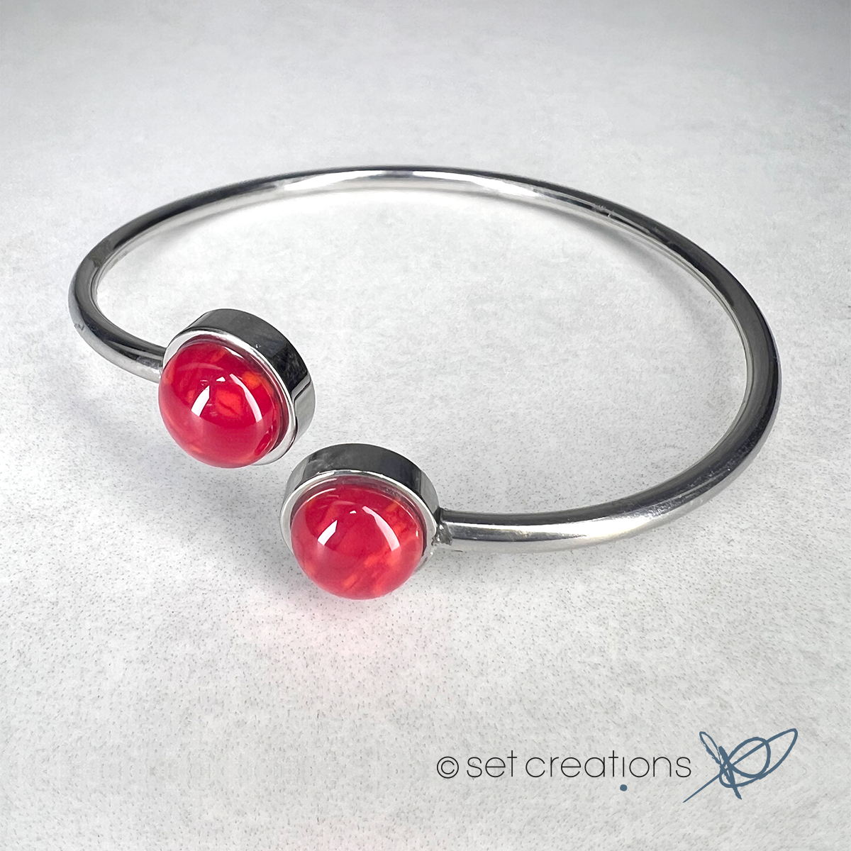 2 x 8mm fused glass circular cabochons set into stainless steel adjustable 2mm thick wire bangles. Cabochon colour: Wild Poppy = bright and mid red marble effect.